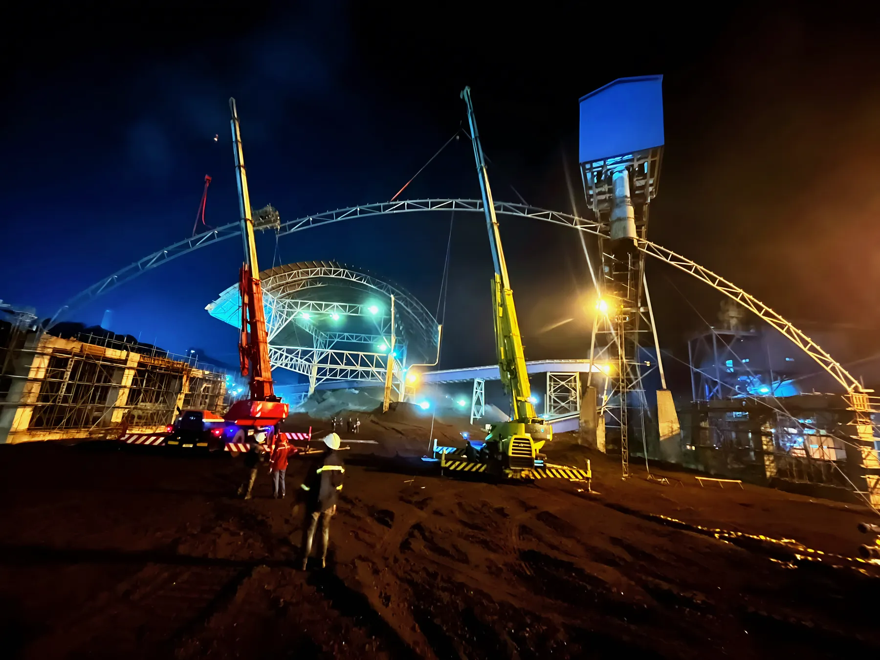 Cranes raising a steel roof structure at night